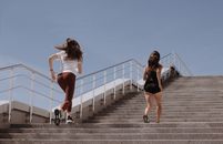 两名女子在晴朗的蓝天下，跑上户外楼梯健身