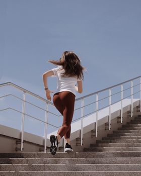 阳光明媚的日子里，一位穿着运动服的健美女性跑上楼梯，展示着积极的生活方式