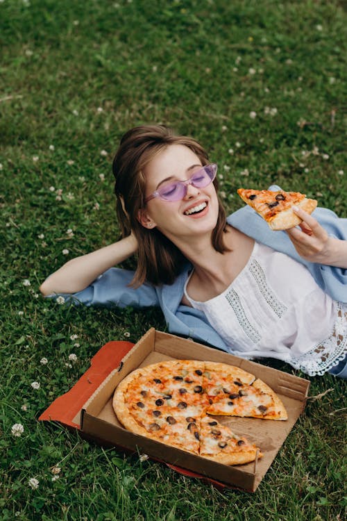 Free Girl in Denim Top Holding Pizza while Lying on Grass Stock Photo