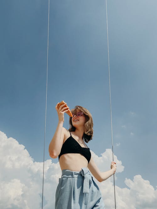 Free Woman in Black Crop Top Holding a Slice of Pizza Stock Photo