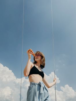 一位穿着露脐上衣的年轻女子，在明亮的蓝天下手拿披萨，尽显休闲与幸福