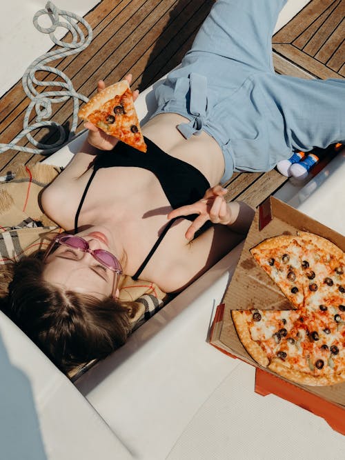 Beautiful Woman in Black Bra Lying with Pizza in Sunlight