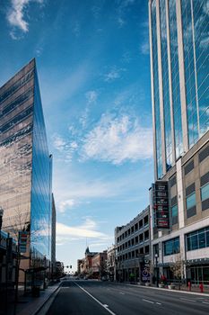 From below of empty asphalt roadway between contemporary multistory building exteriors under colorful blue sky with clouds in city
