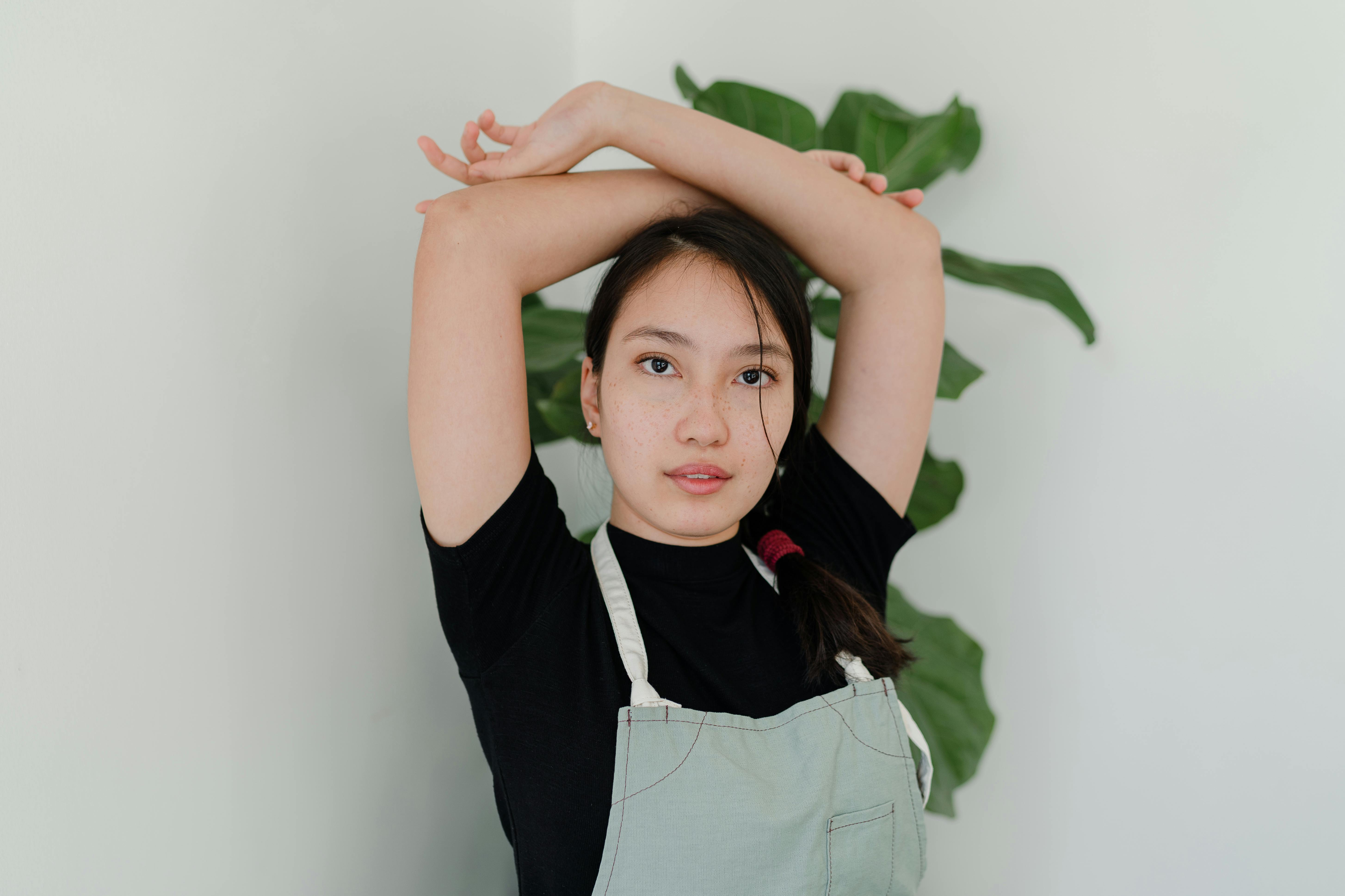 content ethnic woman in apron posing against wall