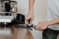 Crop professional barista preparing coffee at wooden counter