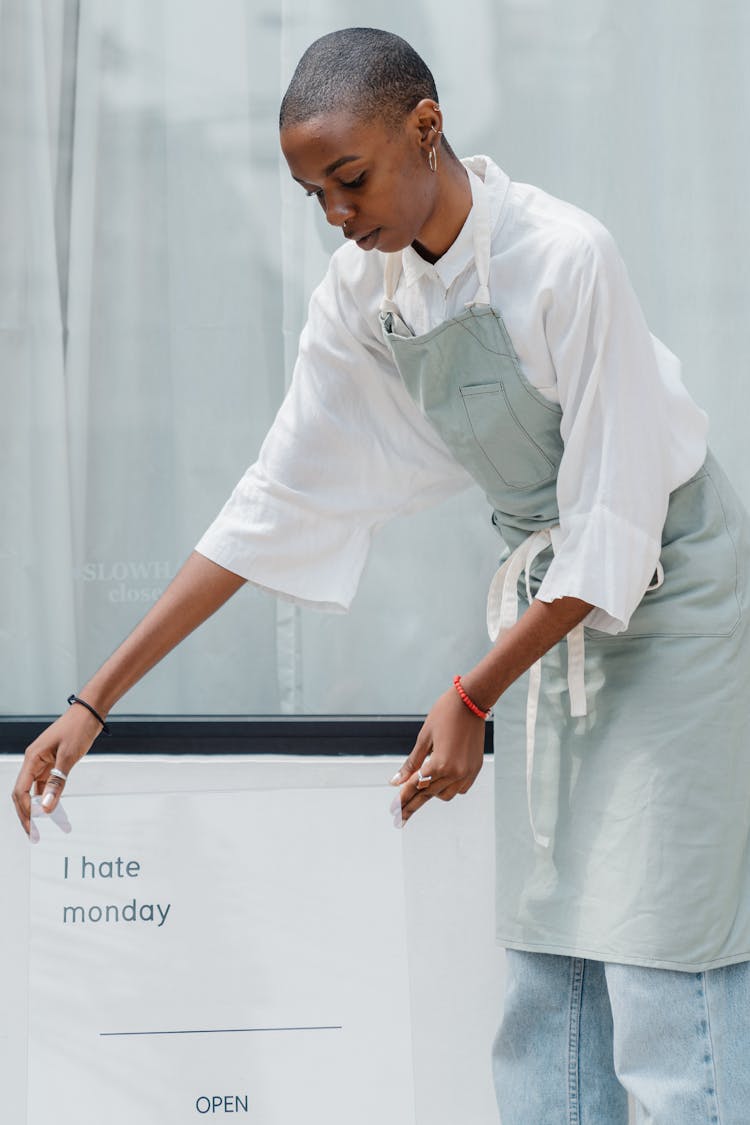 Content Black Female Worker Establishing Signboard Outside Cafe