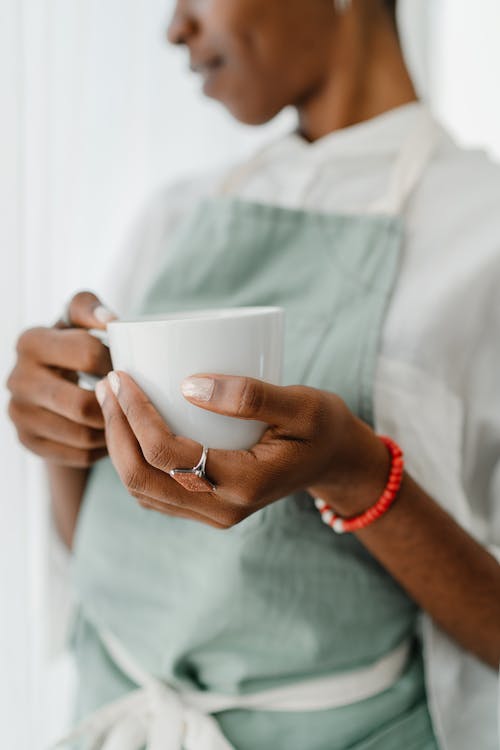 Crop black female barista with coffee mug in coffee shop