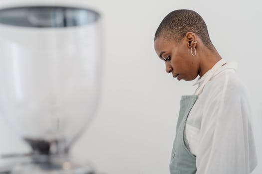 A barista in an apron, focused and introspective, in a modern cafe environment.