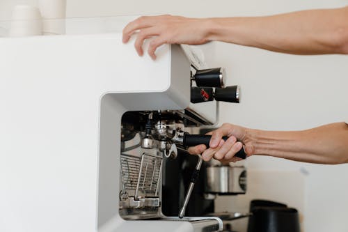 Unrecognizable female bartender adjusting portafilter in coffeemaker for preparing tasty aromatic espresso during work in coffee house