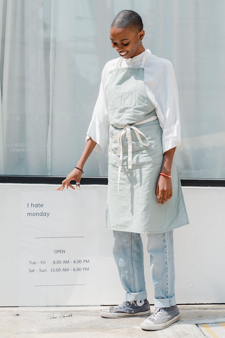 Glad Black Female Worker With Signboard At Entrance Of Cafeteria