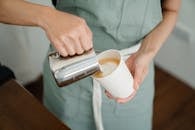 Crop barista pouring milk froth in cappuccino for client