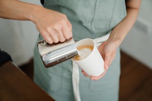 Crop barista pouring milk froth in cappuccino for client