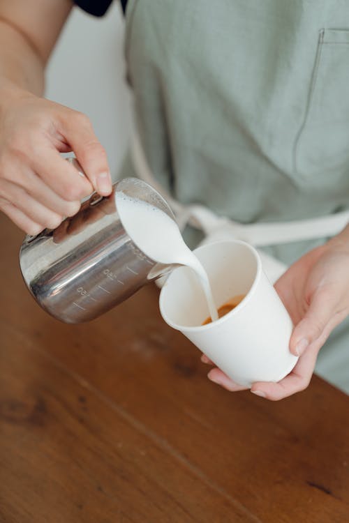 From above of unrecognizable barista pouring milk into cup while preparing cappuccino in modern cafe