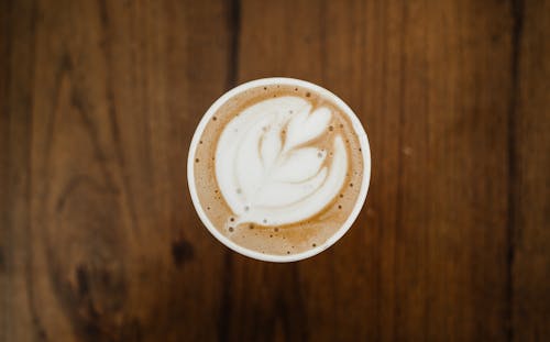 Free Top view of cup of aromatic cappuccino in ceramic cup with white foam poured in form of plant on brown surface Stock Photo