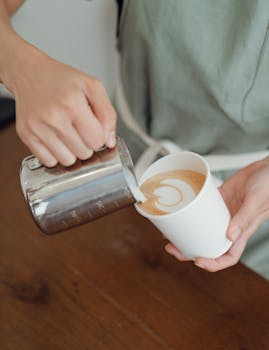 An unrecognizable barista crafting latte art in a coffee shop.