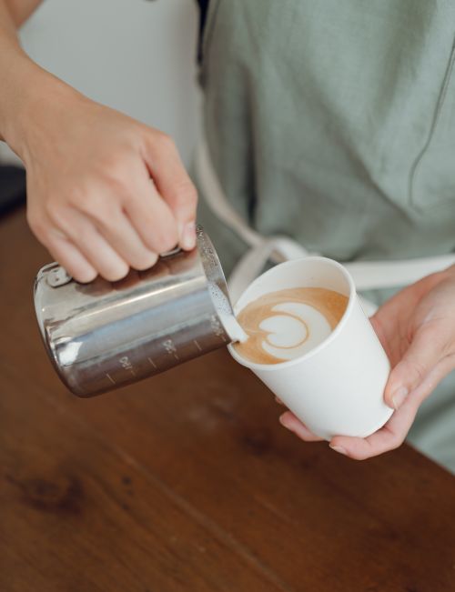 Free Faceless bartender in green apron pouring hot milk froth in hot coffee while making latte art Stock Photo