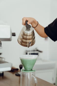 Unrecognizable female barista preparing delicious coffee in glass coffeemaker and pouring hot water during at table in modern cafeteria