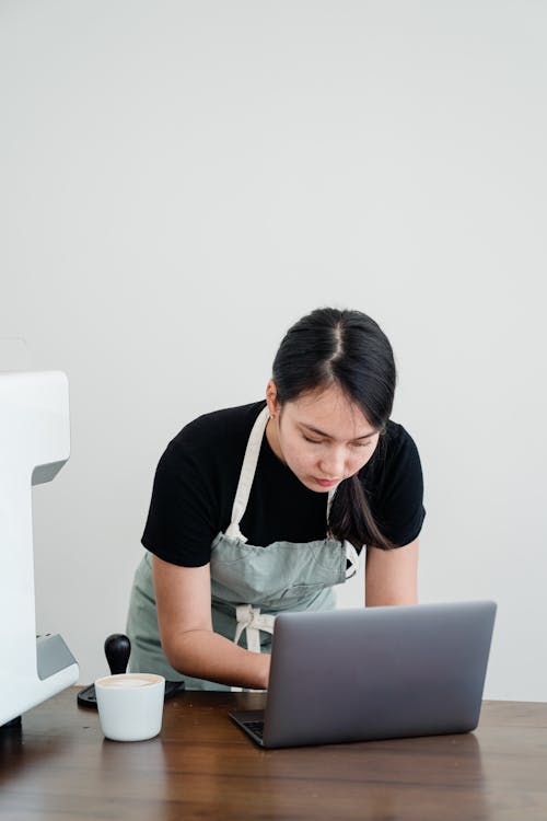 Woman in Black Shirt and Apron While Using Laptop Computer