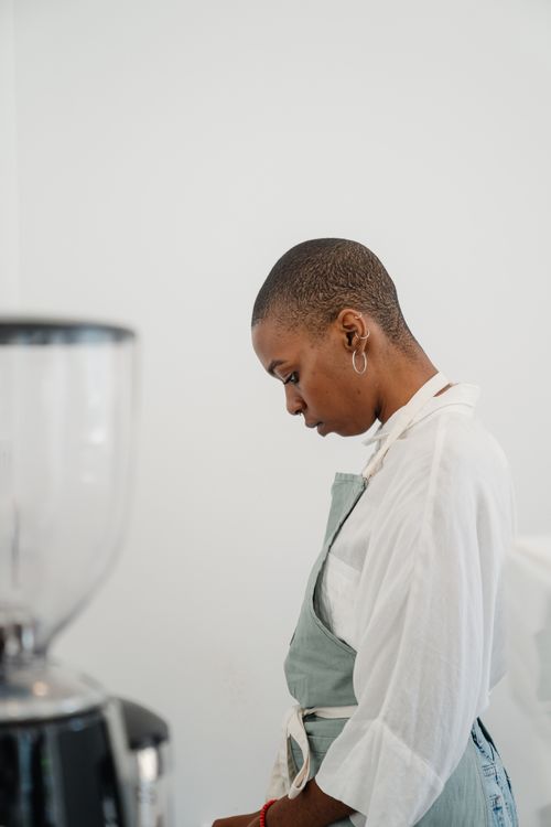 Free A woman in an apron, deep in thought, stands in a minimalist kitchen setting. Stock Photo