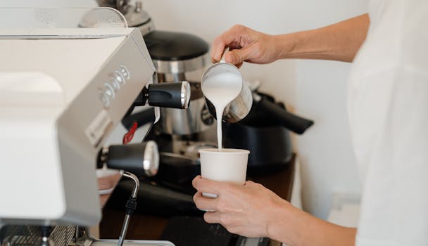 Close-up of a barista pouring steamed milk into a coffee cup using a coffee machine.