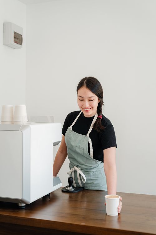 Free Friendly barista serving coffee at a modern cafe counter, wearing an apron. Stock Photo
