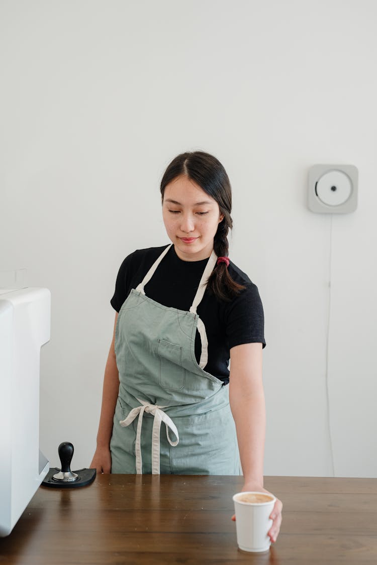 Smiling Young Asian Woman Offering Hot Coffee At Counter