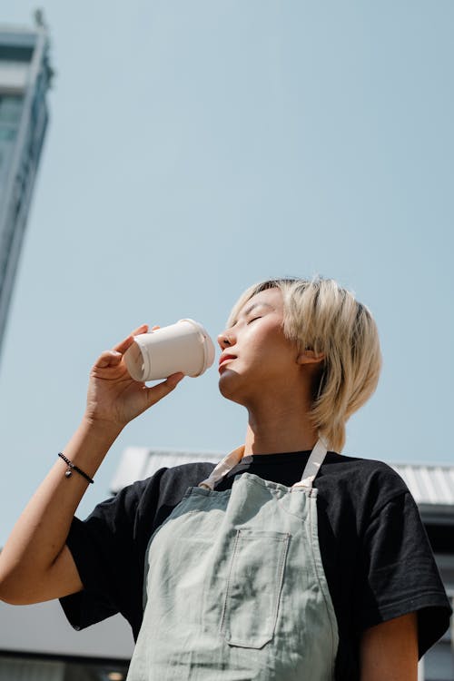 Photo of Woman Wearing Apron While Drinking from Disposable Cup