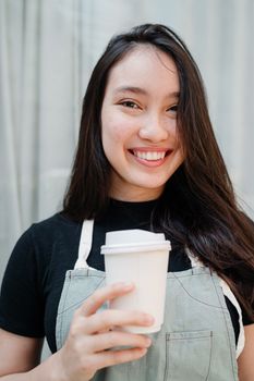 一位面带微笑、身着休闲服装的女子，在室内端着咖啡杯，神情愉悦