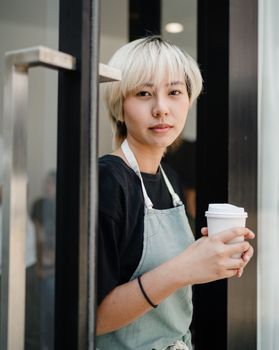一位积极的年轻民族妇女，拿着外卖咖啡，看着照相机的围裙