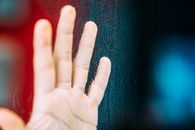 Crop unrecognizable person showing raised hand with calluses illuminated by colorful light near tree trunk