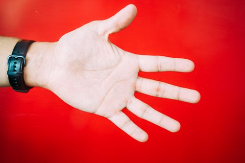 Free A close-up view of an outstretched hand with a black watch against a vibrant red backdrop. Stock Photo