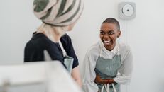 两位女士系着围裙，在休闲的室内环境中分享快乐时光，一同欢笑