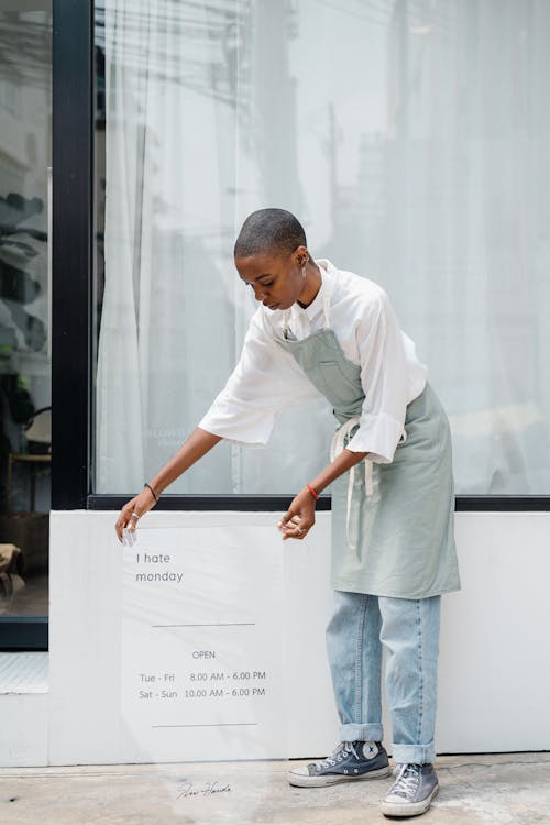 Free African American Waitress With Open Sign Against Modern Cafe Stock Photo