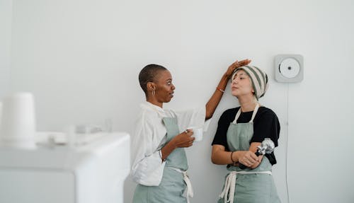 Young black woman drinking coffee and touching head of cheerful female colleague during break at workplace