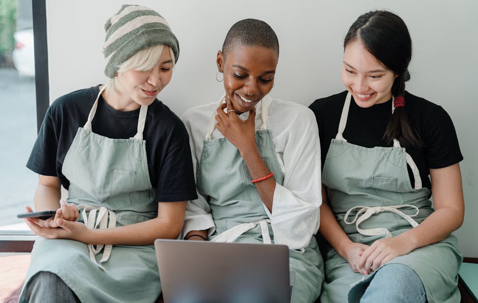 Ultimate Zigbee vs Z-Wave vs Wi-Fi Devices Guide (2025) Three diverse café staff members in aprons enjoy a happy break with a laptop indoors.