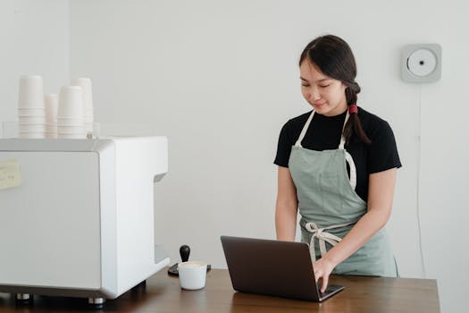 Female barista using a laptop in a modern coffee shop setting, focusing on work.