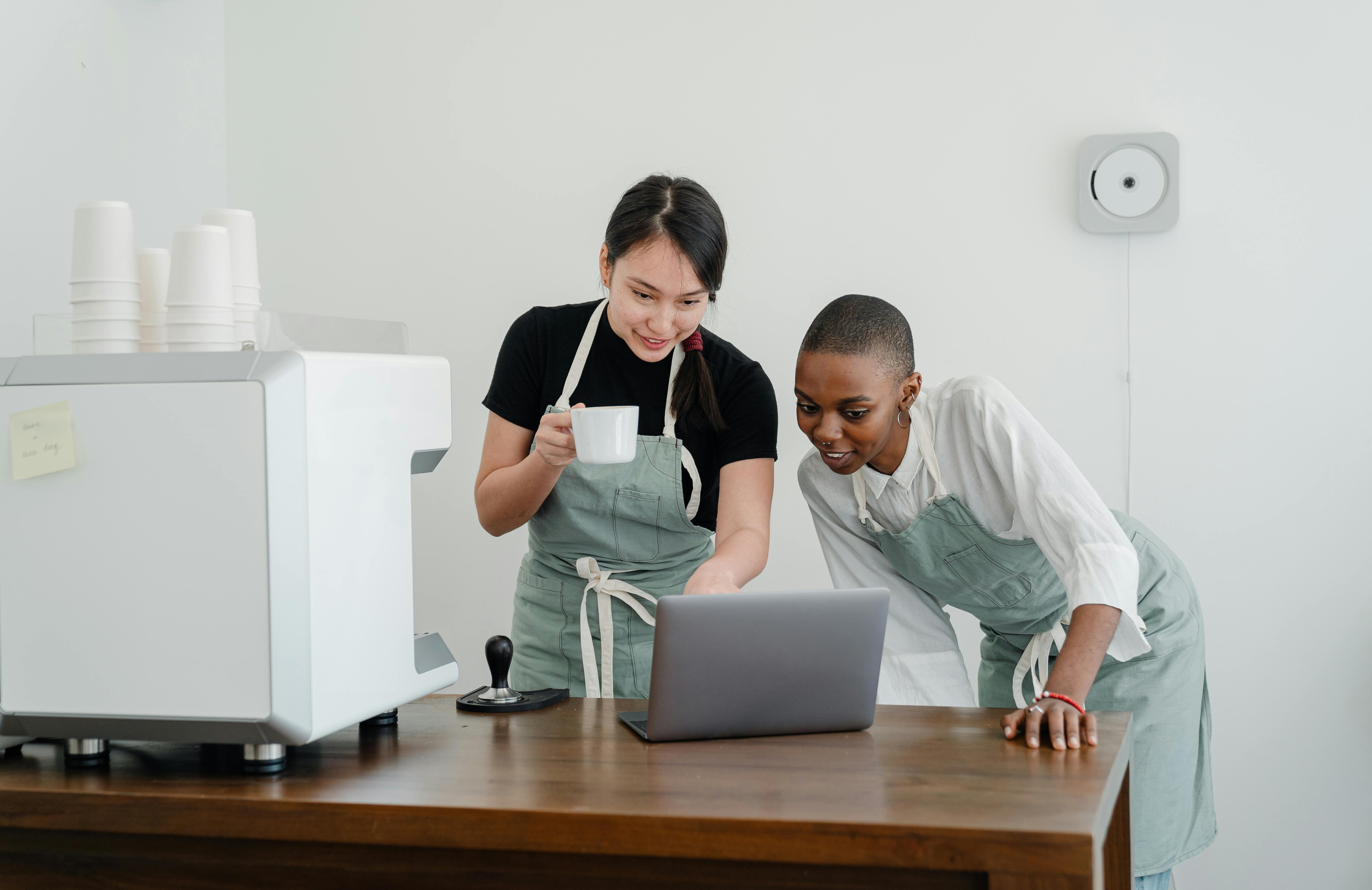 cheerful barista coworkers watching video on laptop during break