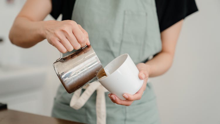 Crop Cafe Worker Pouring Milk From Pitcher To Cup