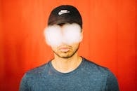 Unrecognizable bearded guy in casual outfit and stylish cap standing with white stains on eyes representing eyeglasses on red background