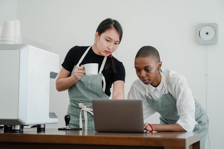 Young Diverse Coworkers At Coffee Shop Using Laptop Together