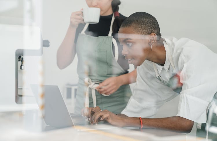 Black Female Barista Together With Colleague Using Laptop At Work