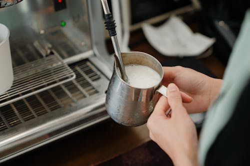 Crop barista whipping milk in stainless steel cup