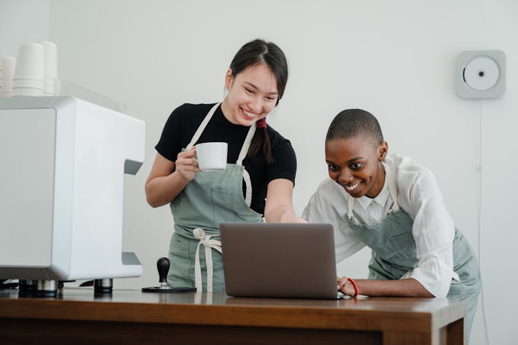 Cheerful Young Multiethnic Coffee House Coworkers Using Laptop During Break