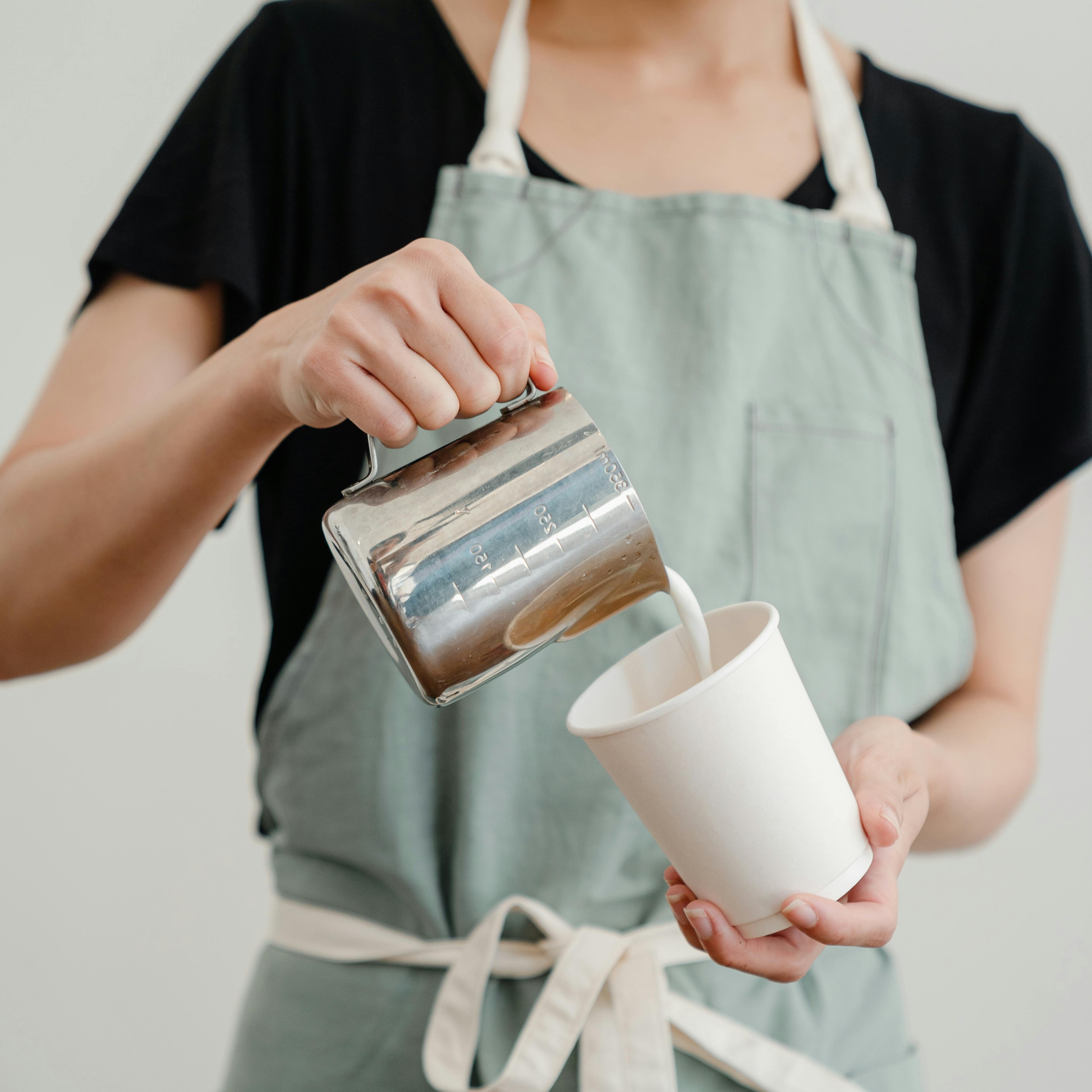 unrecognizable female worker pouring milk into coffee cup