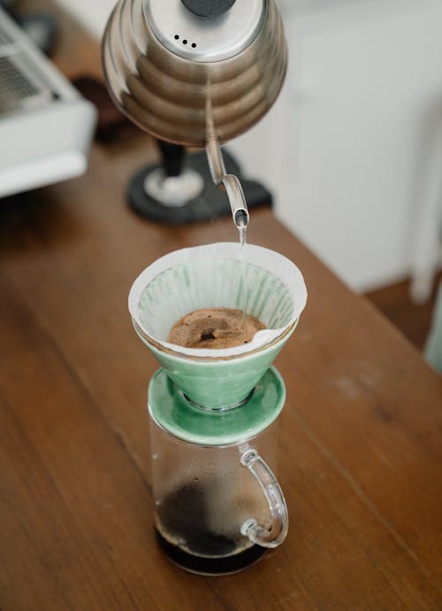 From above of process of dripping water from metal kettle into coffee filter in pour over during alternative coffee brewing