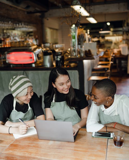 Cheerful colleagues in aprons gathering at table with laptop