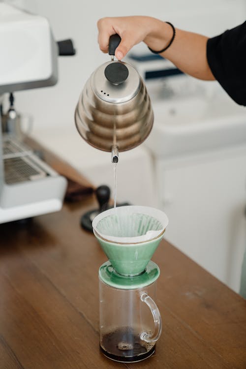 Crop anonymous barista pouring hot water from metal gooseneck kettle into pourover pour over and glass transparent mug in coffee shop