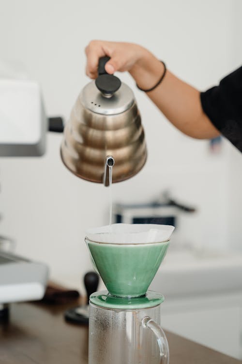 Crop barista pouring water into pourover