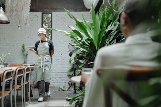 Woman in a modern restaurant setting carrying food, surrounded by lush greenery.