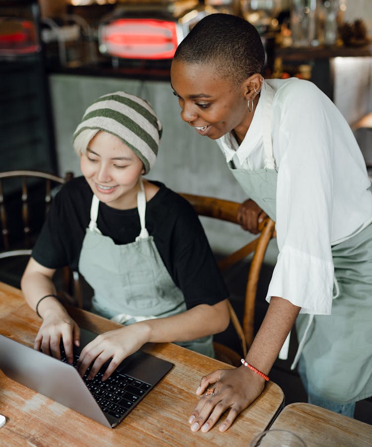 Cheerful Waitresses Typing On Laptop In Cafe